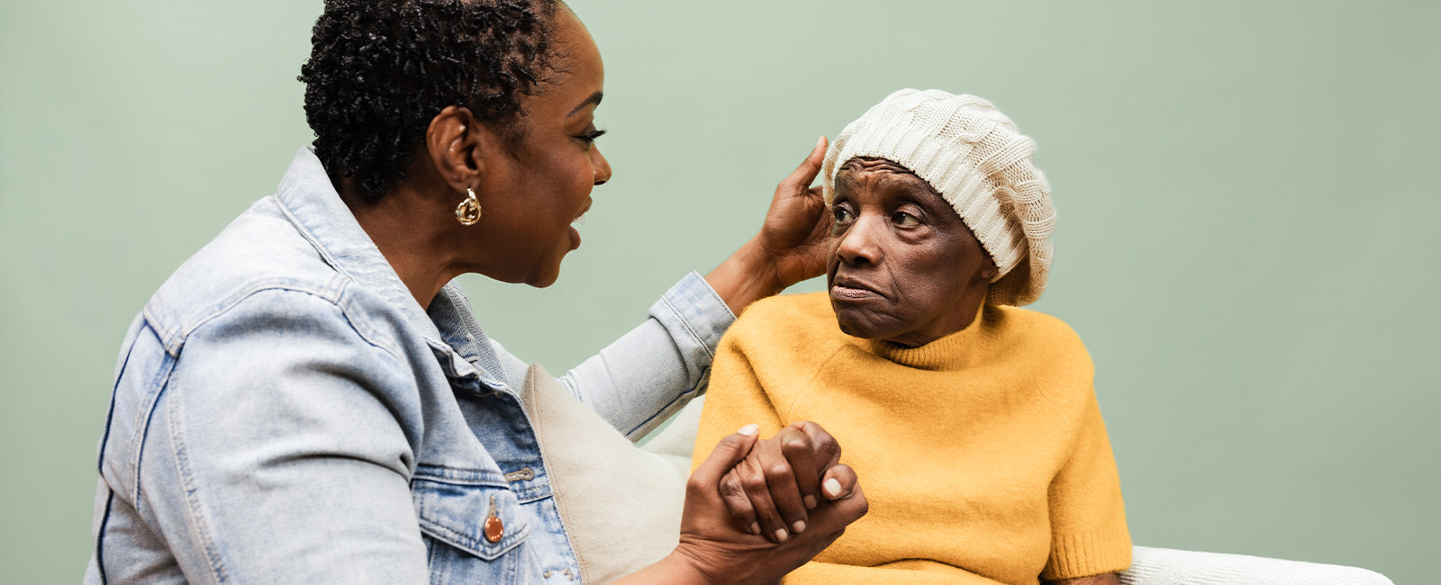 A younger woman gently holding an older woman's hand and face in a moment of comfort