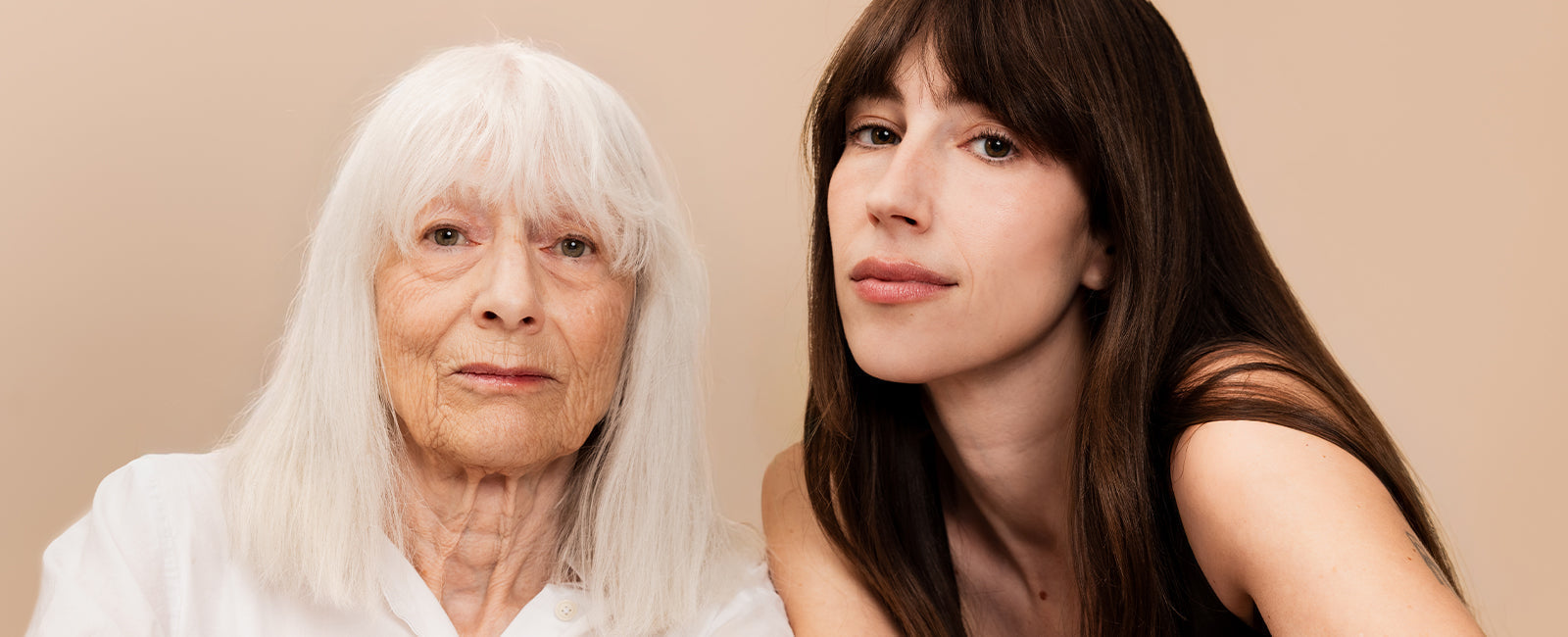 An older woman and a younger woman sitting close together, both looking directly at the camera