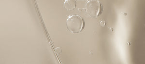 Image of face and body oil with bubbles.  The bubbles are dispersed evenly and provide a textured look to the oil. The background is a neutral color that accentuates the golden color of the oil.