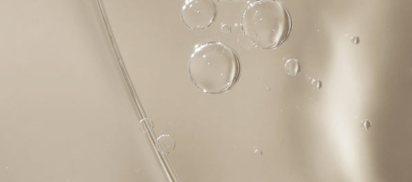 Image of face and body oil with bubbles.  The bubbles are dispersed evenly and provide a textured look to the oil. The background is a neutral color that accentuates the golden color of the oil.