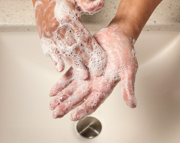 Lathered hands being washed over a white bathroom sink.