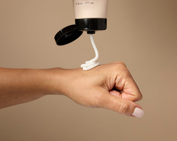 Hand applying cream against a beige background