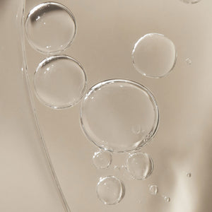 Image of face and body oil with bubbles.  The bubbles are dispersed evenly and provide a textured look to the oil. The background is a neutral color that accentuates the golden color of the oil.