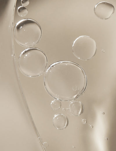 Close-up photo of body oil with bubbles on its surface, on a plain background.