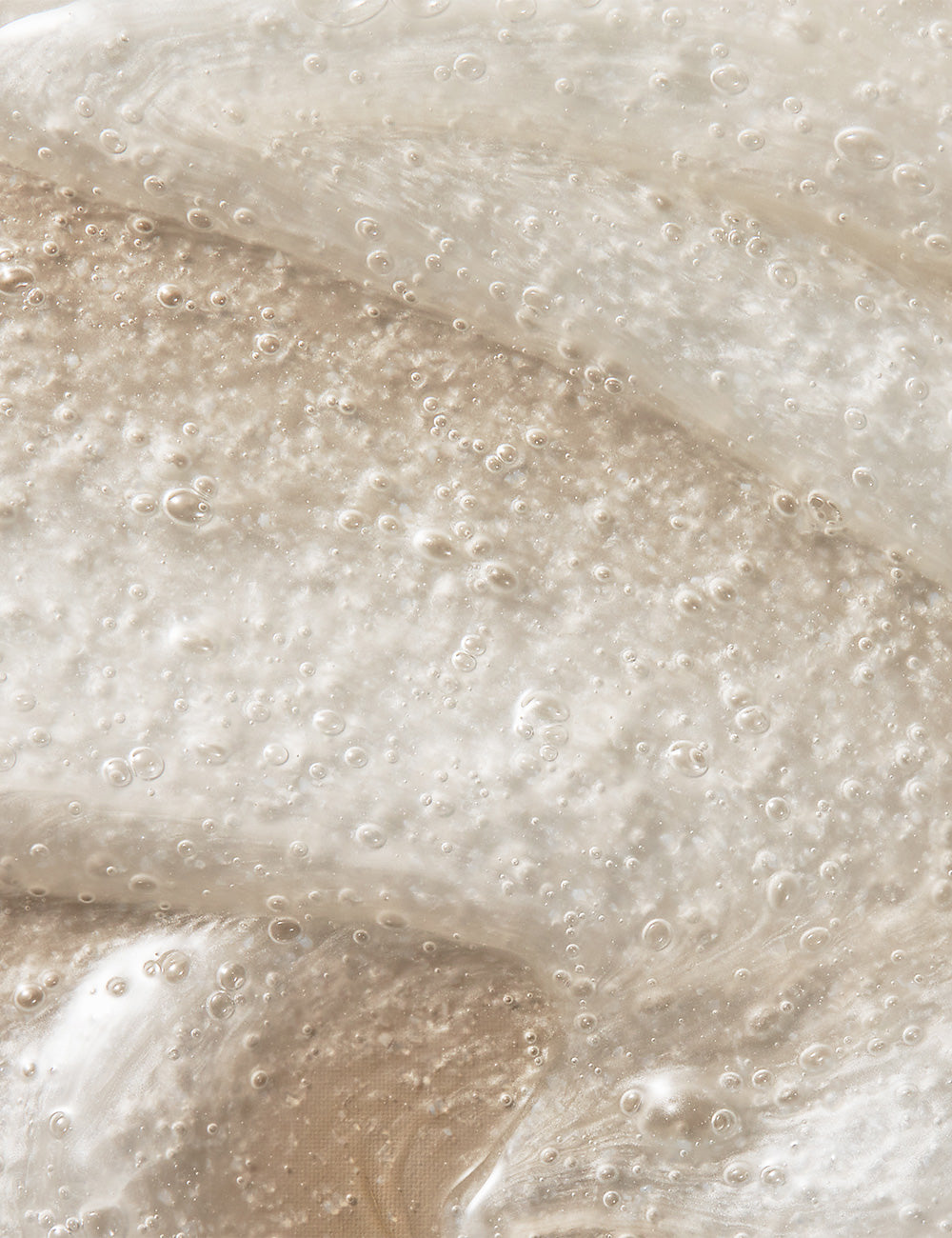 Close-up photo of exfoliator cream with small granules on a tan background.