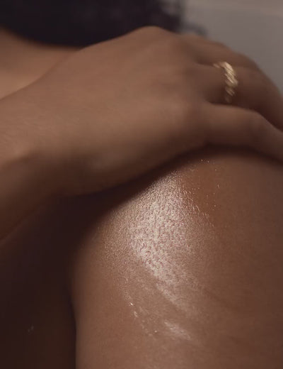 A video of a woman's hand rubbing body oil onto her shoulder