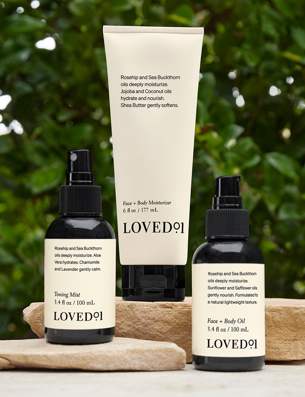 A collection of skincare products sitting on tan stones with green foliage in the background.