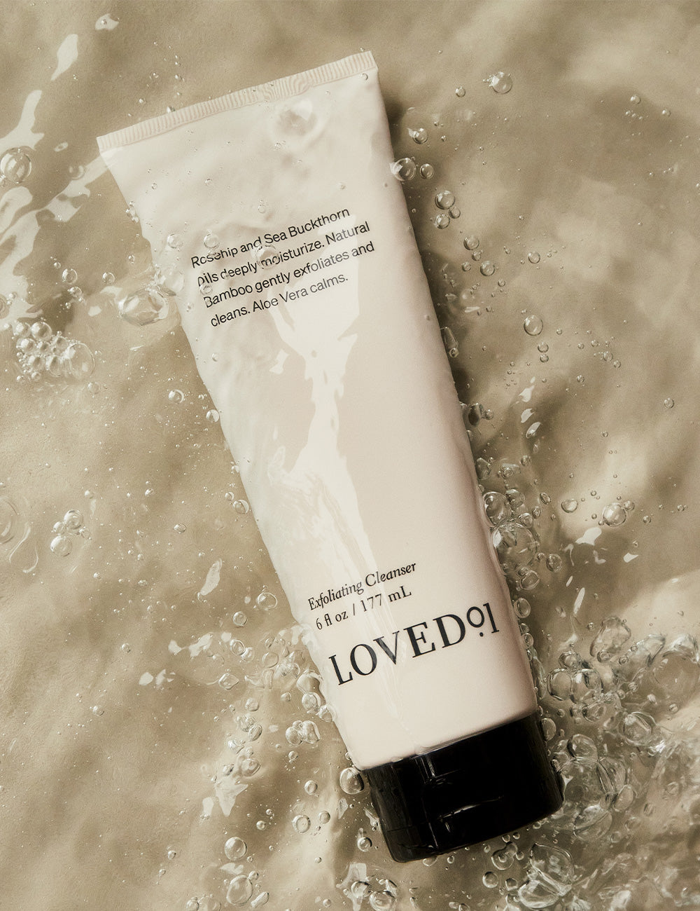 A tube of exfoliating cleanser with water droplets running down the sides, on a tan background.