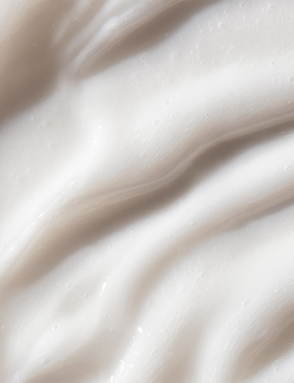 Close-up photo of the creamy and white texture of body wash with small bubbles, on a plain background.