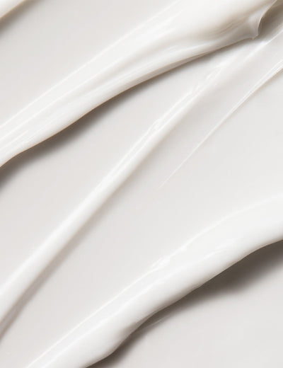 Close-up photo of a moisturizer being swirled or applied, with a creamy white texture, on a plain background.