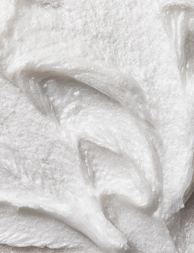Close-up photo of the creamy and white texture of shaving cream with visible brush strokes, on a plain background.